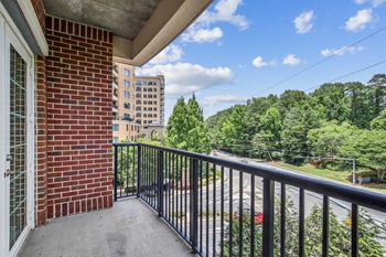 A balcony with a black railing overlooks a street with cars and trees.